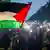 Blick auf viele Menschen bei einer Demonstration gegen den Gaza-Krieg in der Dämmerung im Zentrum Berlins. Zum Zeichen ihrer Solidarität schalteten viele Menschen die Taschenlampen ihrer Smartphones ein. In der ersten Reihe schwenkt ein Jugendlicher die Palästina-Fahne in den Farben Schwarz, Weiß, Grün und Rot
