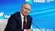 Vladimir Putin, in a black jacket, sits in front of a thin microphone against a bright blue background with the logo "Valdai" (October 2025)