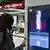 A woman scans a QR-code on a screen with an AI-generated virtual assistant with her smartphone at the BER Airport train station