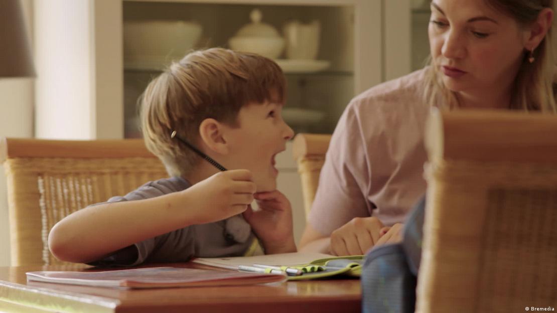 Una madre está sentada a la mesa con su hijo haciendo los deberes. El niño mira a su madre y le grita.