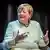 Angela Merkel sitzt lächelnd und gestikulierend vor einem dunklen Vorhang