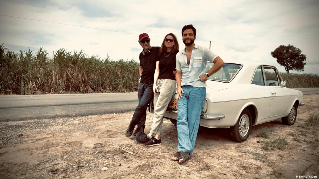 Kleber Mendonça, Emilie Lesclaux e Wagner Moura encostados em um carro parado na beira da estrada