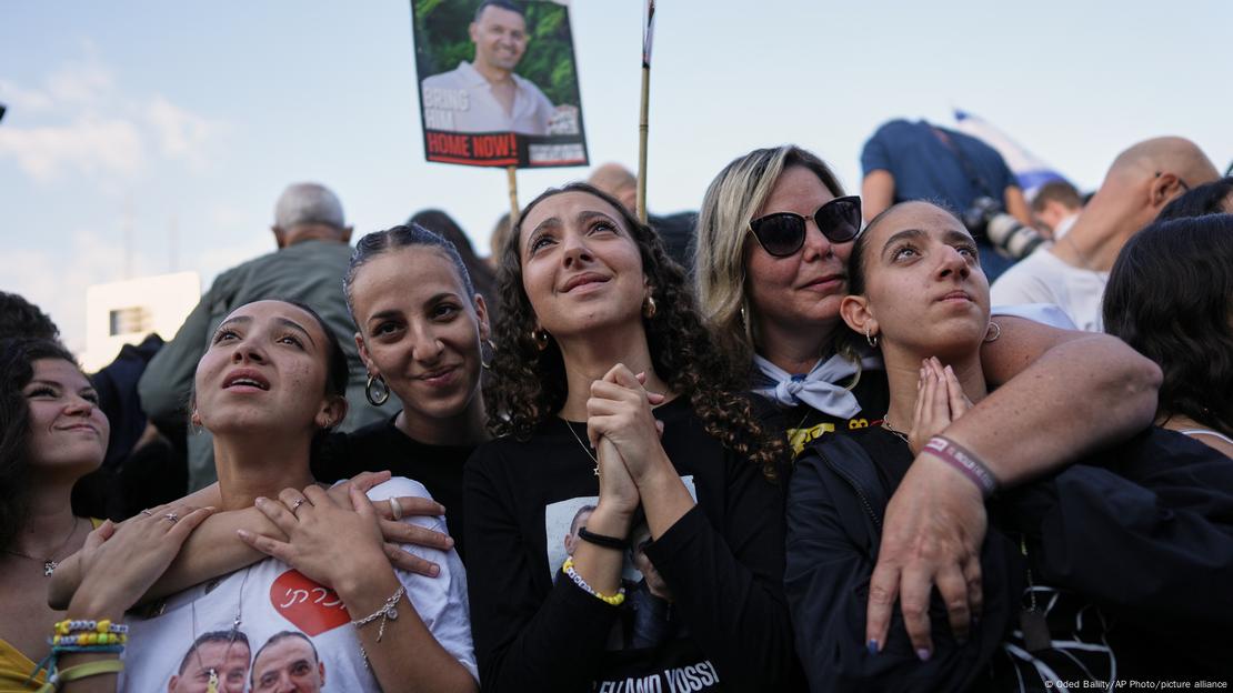 Pessoas emocionadas se abraçam, com cartaz com foto de refém ao fundo Pessoas emocionadas se abraçam, com cartaz com foto de refém ao fundo