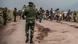 People and vehicles on road near Kibumba in DRC with Congolese soldiers visible in foreground People and vehicles on road near Kibumba in DRC with Congolese soldiers visible in foreground