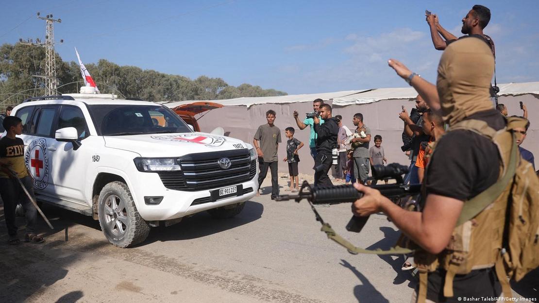 Territorios Palestinos, Deir al-Balah, 2025 | Un vehículo blanco y rojo de la Cruz Roja, avanza , flanuqeado por hombres y niños curiosos, militantes armados y enmascarados, así como al menos dos hombres que filman la escena, mientras Hamás libera al segundo grupo de rehenes israelíes devueltos a Israel.