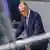 Friedrich Merz, man talking in parliament on right, with blurred reflection on left