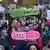 A crowd of people, most of them white, hold up makeshift pink and green signs that read 'We are the cityscape' in German