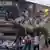 Young people in Tehran walk by a mural showing happy cartoon children