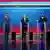 Three men, who clean-shaven, one bearded, standing at transparent pulpits in front of a blue and red illuminated background: Andrew Cuomo (L), Curtis Sliwa (C) and Zohran Mamdani (R)