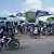 Crowd of people, some on motorbikes, at a gas station