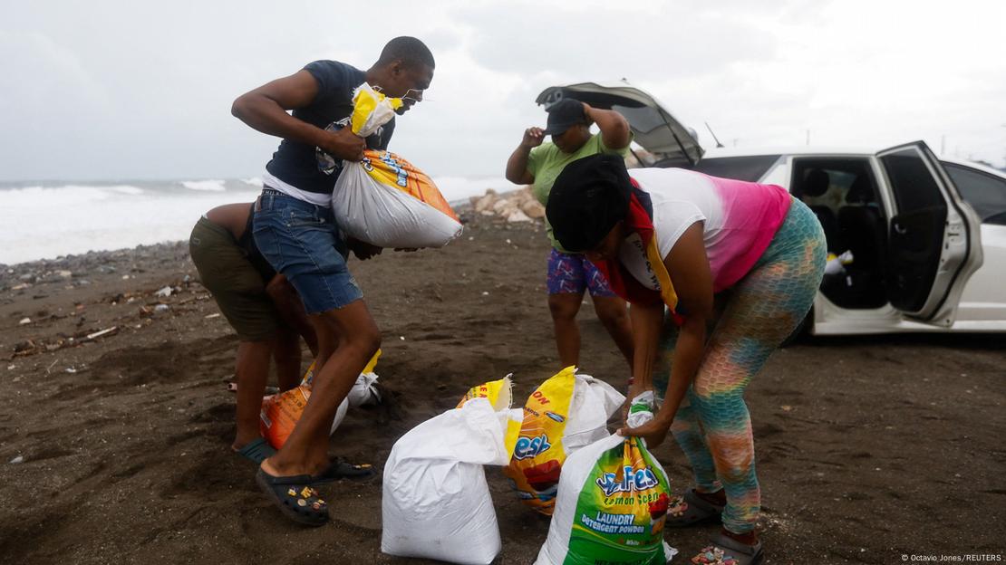 Un grupo de personas acarrea bolsas de arena en Jamaica para frenar la llegada del agua ante la alerta por el huracán Melissa.