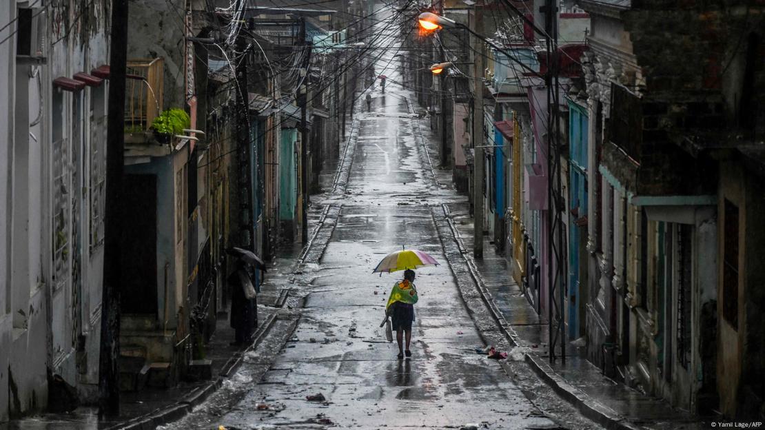 Pessoa caminha solitária com guarda-chuva em uma rua de Santiago de Cuba Pessoa caminha solitária com guarda-chuva em uma rua de Santiago de Cuba