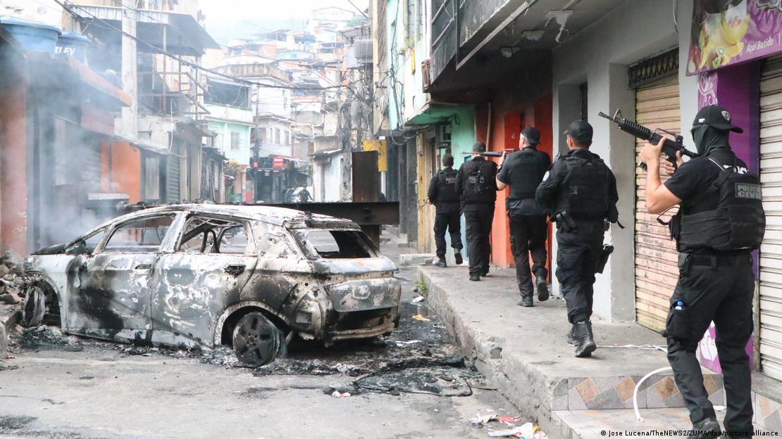 Un grupo de agentes camina por una calle en Río de Janeiro. Al lado se aprecia un vehículo incendiado.