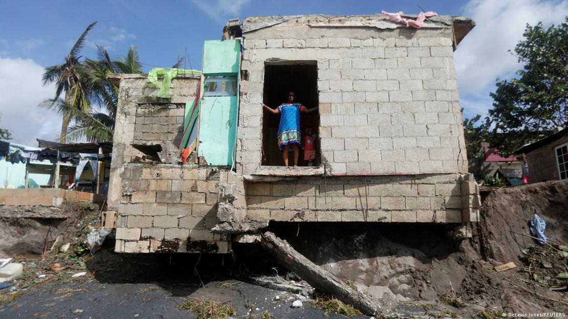 Una mujer está de pie dentro de una casa destruida en medio de un sitio afectado por el paso de un huracán.