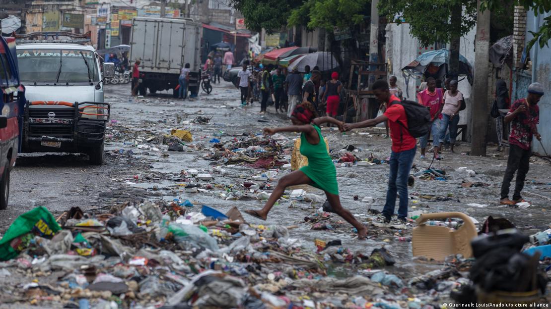 Una pareja intenta saltar en medio de la basura y los restos dejados por las inundaciones en Puerto Príncipe.
