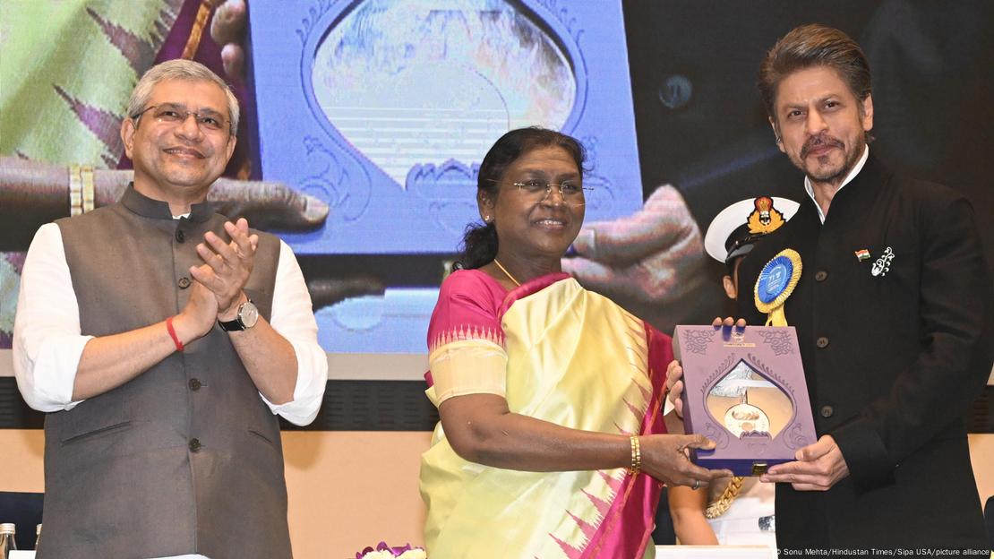 Picture of two men and a woman. The woman is presenting an award to one of the men. 