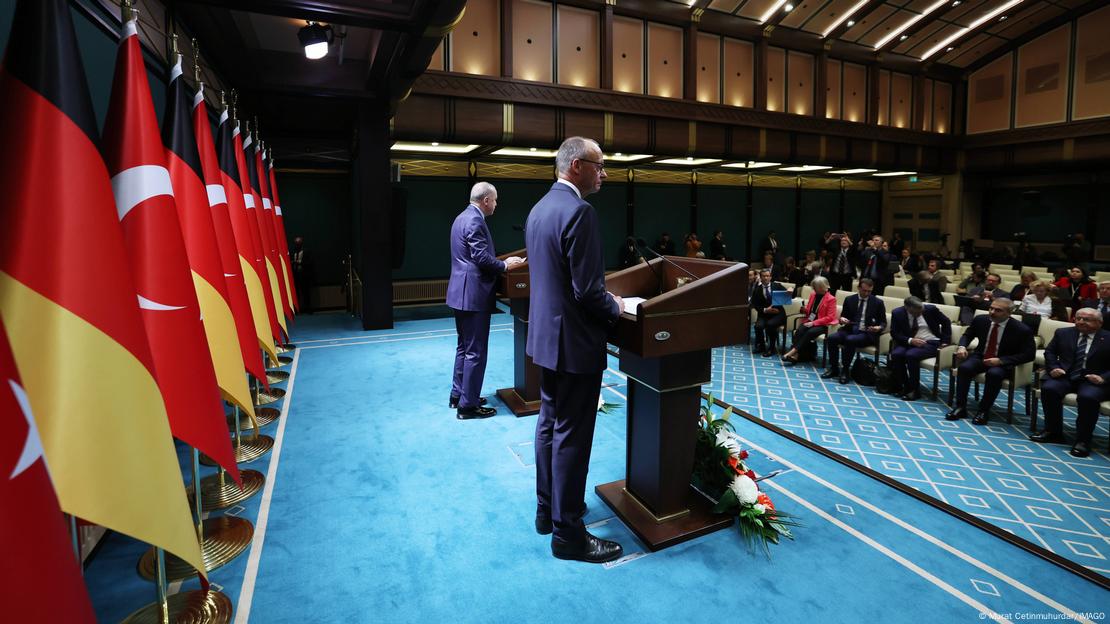 Ortak basın toplantısındaki Merz ve Erdoğan'ın yandan çekilmiş bir fotoğrafı. Arkalarında Türk ve Alman bayrakları var.