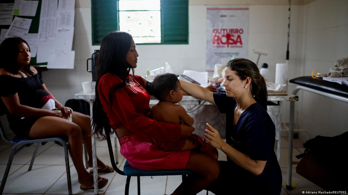 Médica em consultório atende mulher com bebê