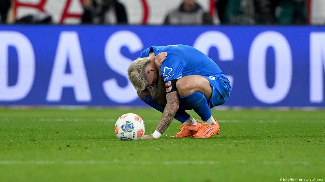 Bayer Leverkusens Robert Andrich hockt im Spiel beim FC Bayern München am Boden und hält sich einen Arm vor das Gesicht