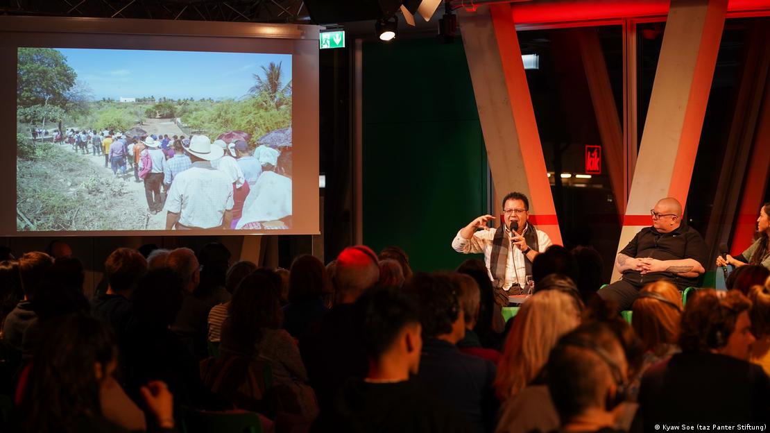 Periodista habla al público mientras muestra fotos de su trabajo de campo.