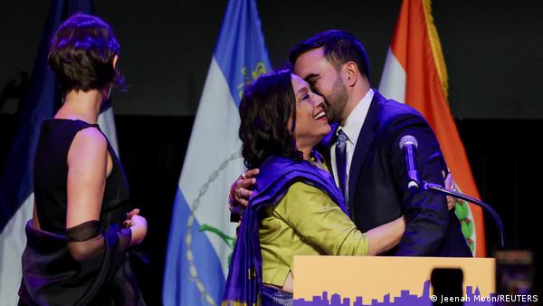 Seçim zaferinin ardından kürsüde annesi Mira Nair'e sarılan ve öpen Zohran Mamdani. Annesinin güldüğü görülüyor. Mamdani'nin eşi Rama Duwaji de yanlarında.