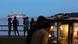 Menschen stehen an einem Strand, im Hintergrund zwei hell erleuchtete Kreuzfahrtschiffe vor Anker an einem langen Pier. Brasilien Belém 2025 | Menschen am Brasília Beach vor COP30-Delegationsunterkünften Menschen stehen an einem Strand, im Hintergrund zwei hell erleuchtete Kreuzfahrtschiffe vor Anker an einem langen Pier. Brasilien Belém 2025 | Menschen am Brasília Beach vor COP30-Delegationsunterkünften