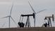 Oil derricks and wind mills are juxtaposed in a field Oil derricks and wind mills are juxtaposed in a field
