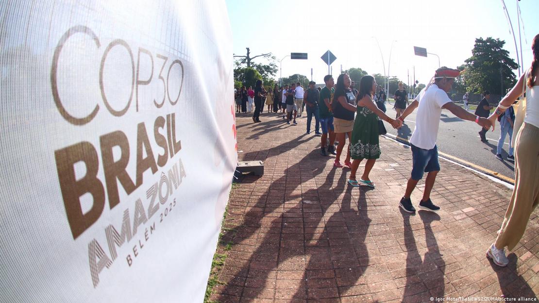 Junge Menschen bilden eine Menschenkette vor einem Schild der COP30-Klimakonferenz im brasilianischen Belém 