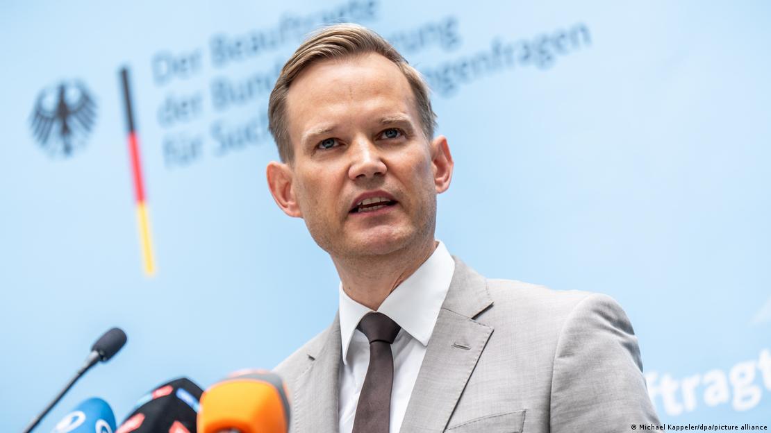 Germany's Drug Commissioner Hendrik Streeck, a young man in a suit and tie, speaking into several microphones at a press conference