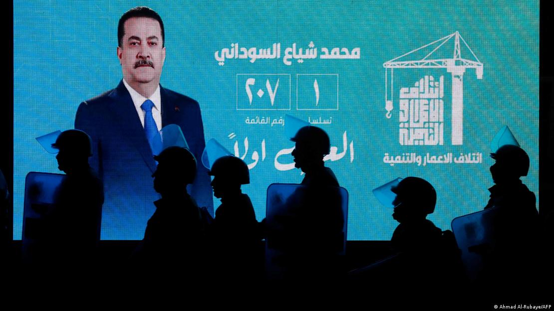 Mohammed Shia al-Sudani auf einer Videoleinwand, davor Schatten von Sicherheitskräften