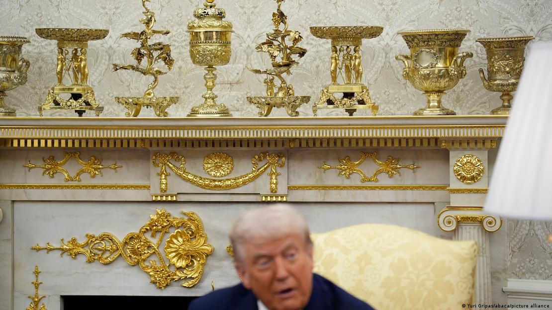 Donald Trump, Oval Ofis'teki şöminenin önünde görülüyor. Şömine üzerindeki altın süslemeler dikkat çekiyor