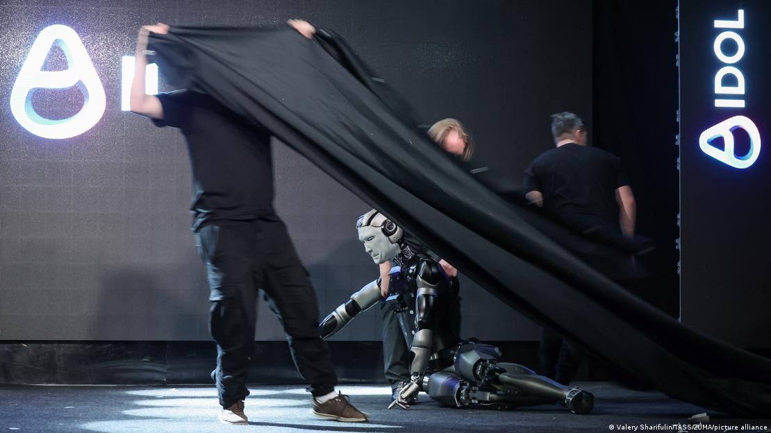 Personal técnico intentó ocultar con una cortina negra al fallido robot AIdol tras su caída en el escenario del Centro Yarovit. Personal técnico intentó ocultar con una cortina negra al fallido robot AIdol tras su caída en el escenario del Centro Yarovit.