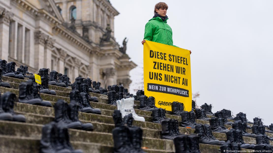 Ein Aktivist von Greenpeace hält vor dem Reichstagsgebäude ein Schild mit der Aufschrift "Diese Stiefel ziehen wir uns nicht an. Nein zur Wehrpflicht" hoch, auf der Treppe stehen viele Paare schwarze Bundeswehrstiefel
