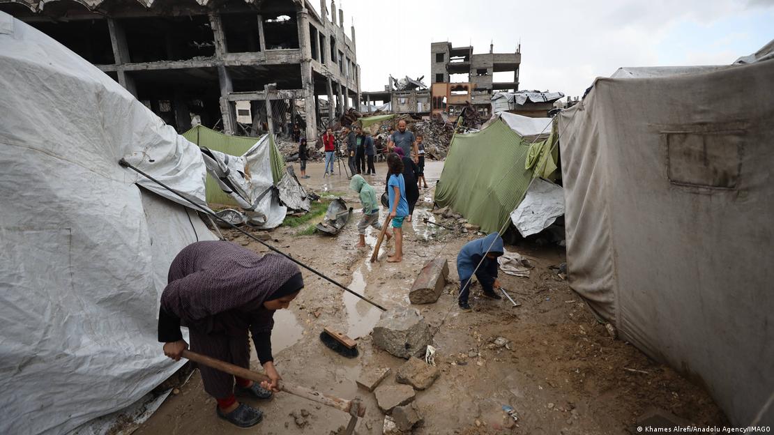 غزہ، خیمہ بستی کی مکین خاتون اپنے خیمے کے پاس بارش کا پانی صاف کرتے ہوئے۔ 