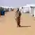 A woman walks in the sand between two rows of white refugee tents in Sudan