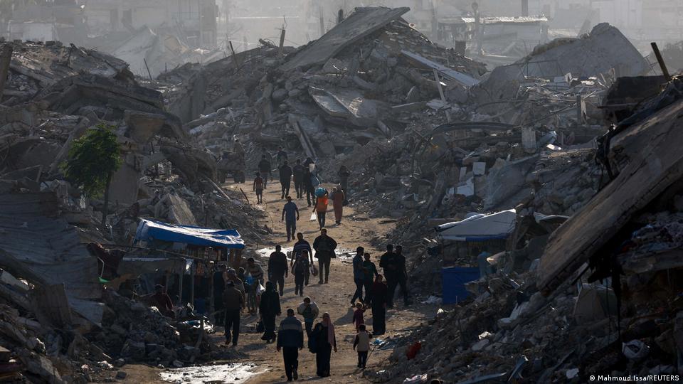 غزہ پٹی کے شمالی حصے میں تباہ شدہ عمارات کے ملبے کے درمیان بنے راستے سے پیدل گزرتے ہوئے فلسطینی