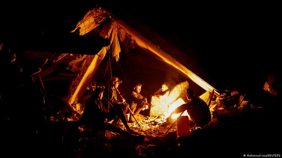 رات کے وقت سردی کی وجہ سے ایک خیمے میں آگ جلا کر بیٹھے ہوئے فلسطینی