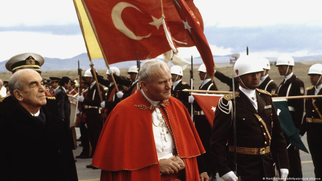 Juan Pablo II, con militares detrás de él, que ondean una bandera turca.