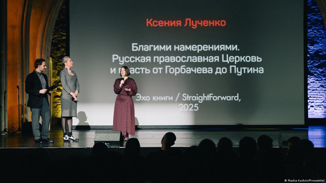 На сцене вручается награда за книгу, стоит ведущий церемонии, председательница жюри, победительница говорит в микрофон На сцене вручается награда за книгу, стоит ведущий церемонии, председательница жюри, победительница говорит в микрофон