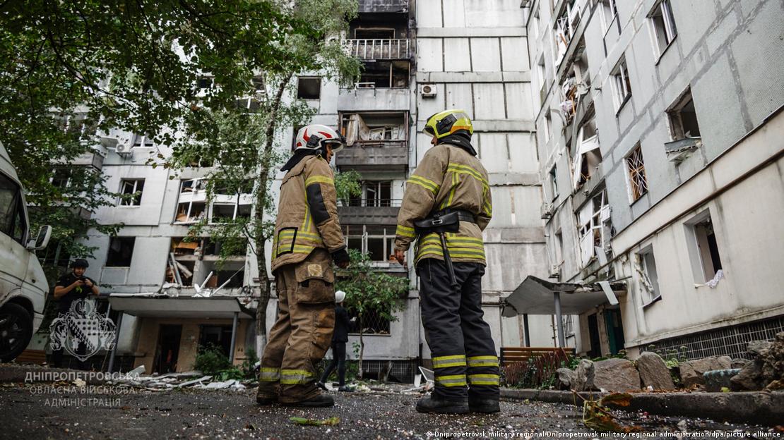 Dos bomberos con un edificio de viviendas visiblemente dañado al fondo el pasado 20 de septiembre.
