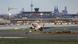 The runway of an airport with a plane taking off and the terminal in the background The runway of an airport with a plane taking off and the terminal in the background