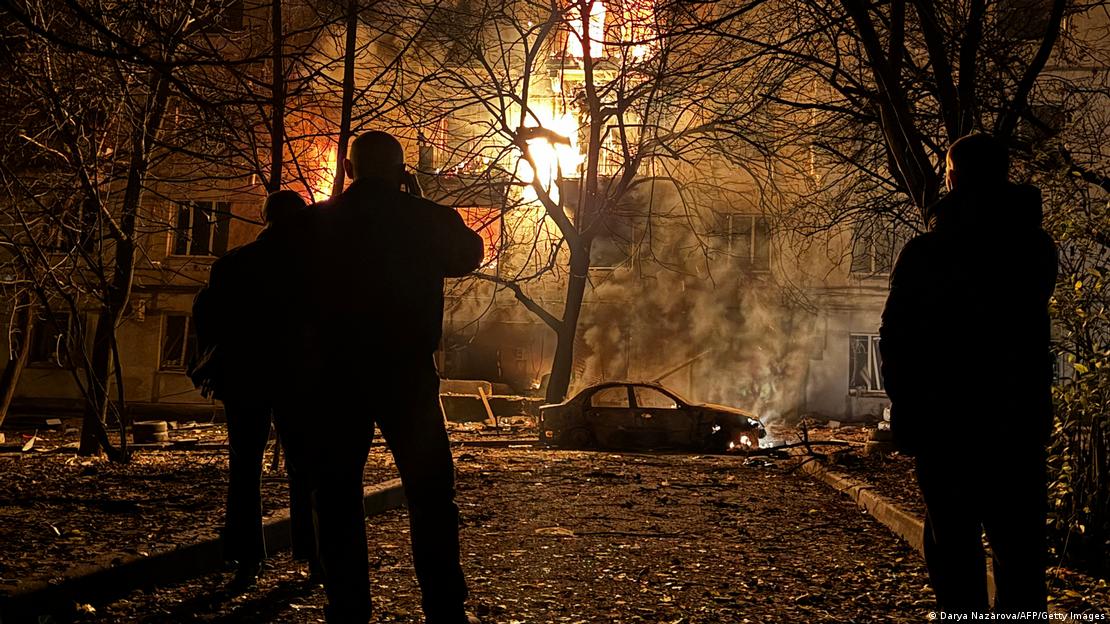 Ein brennendes Wohngebäude, davor drei Anwohner