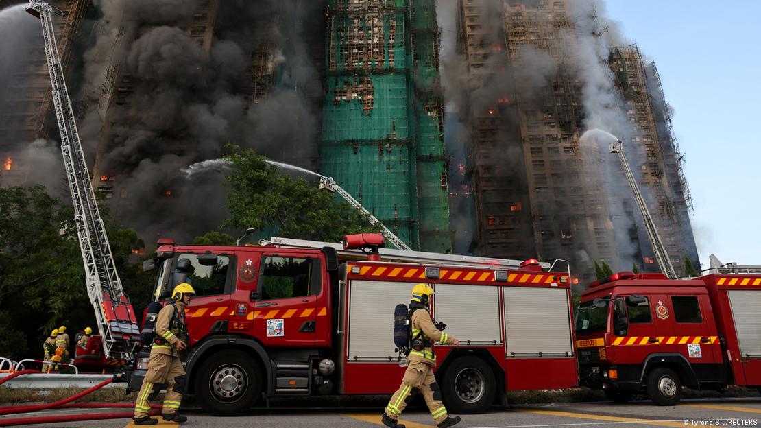 Bomberos junto a carros de extinción de incendios intentan apagar las llamas en los andamios de bambú en varios edificios en Hong Kong.