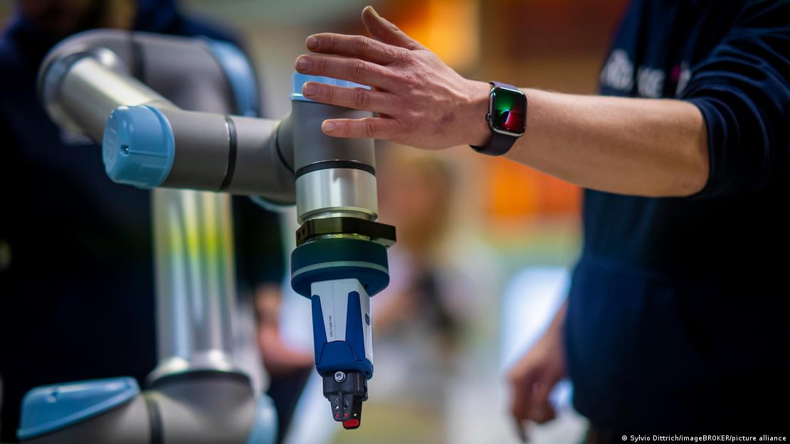 Una persona opera con su brazo el brazo mecánico de un robot industrial
