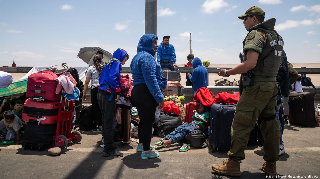 Un grupo de venezolanos con maletas espera a la orilla de una carretera. Una mujer conversa con un carabinero.