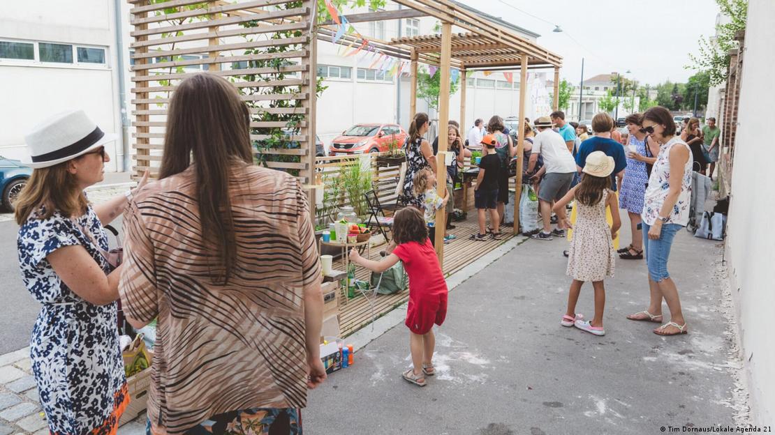 Pessoas na calçada, com crianças brincando, sob uma pérgula