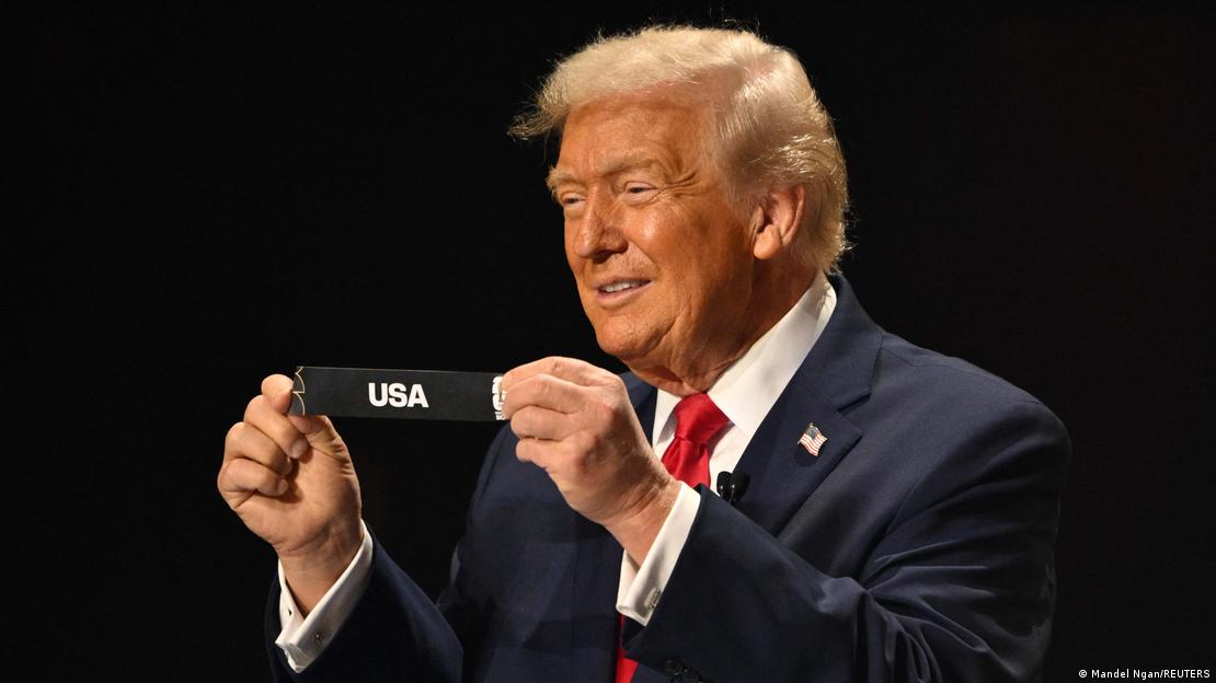 ABD Başkanı Donald Trump, elinde "USA" yazılı kağıt şeridi, gülümseyerek kameralara gösteriyor