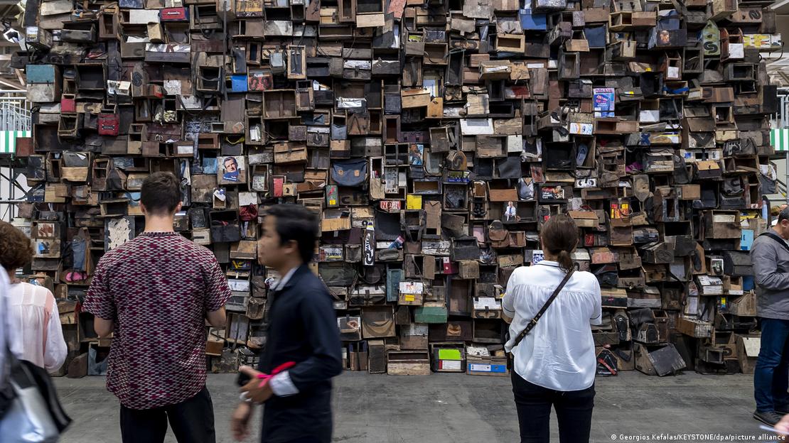 Οι άνθρωποι στέκονται μπροστά από έναν πανύψηλο τοίχο από μικρά ξύλινα κουτιά