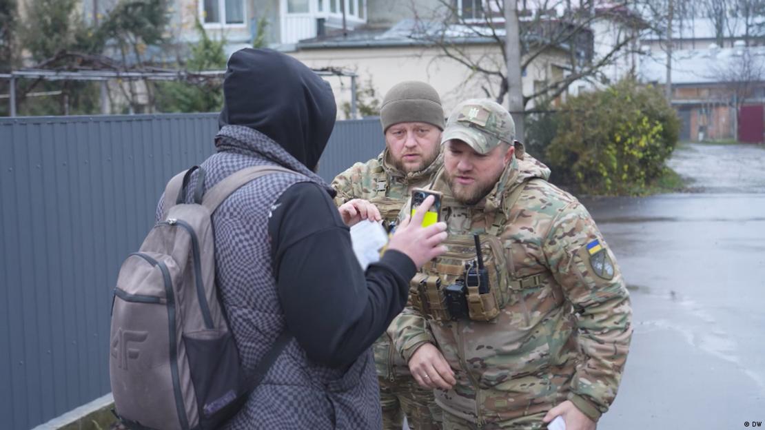Zwei ukrainische Mobilisierungsoffiziere überprüfen auf einer ukrainischen Straße die Ausweispapiere eines Mannes im wehrpflichtigen Alter. 