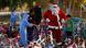 A man dressed as Santa Clause stands in the middle of a gorup of children and bicycles